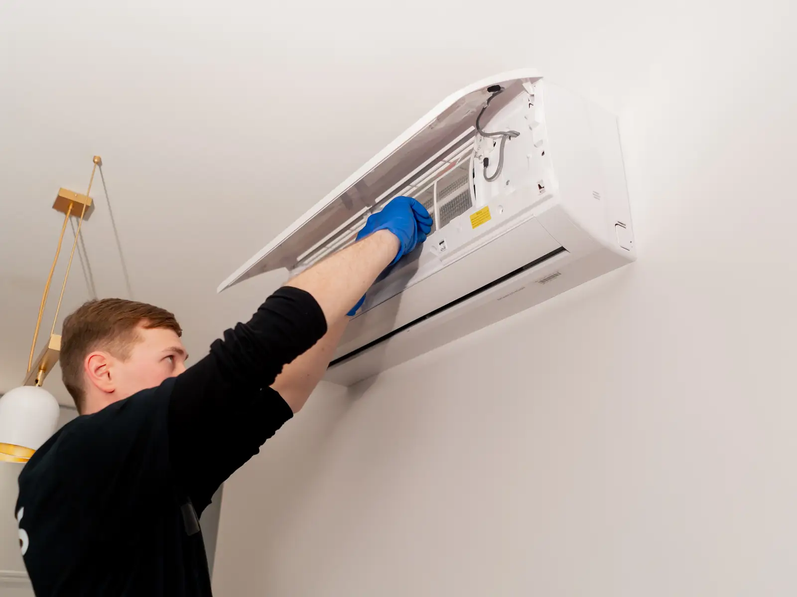 Technicien nettoyant une unité murale de climatisation avant le traitement désinfectant