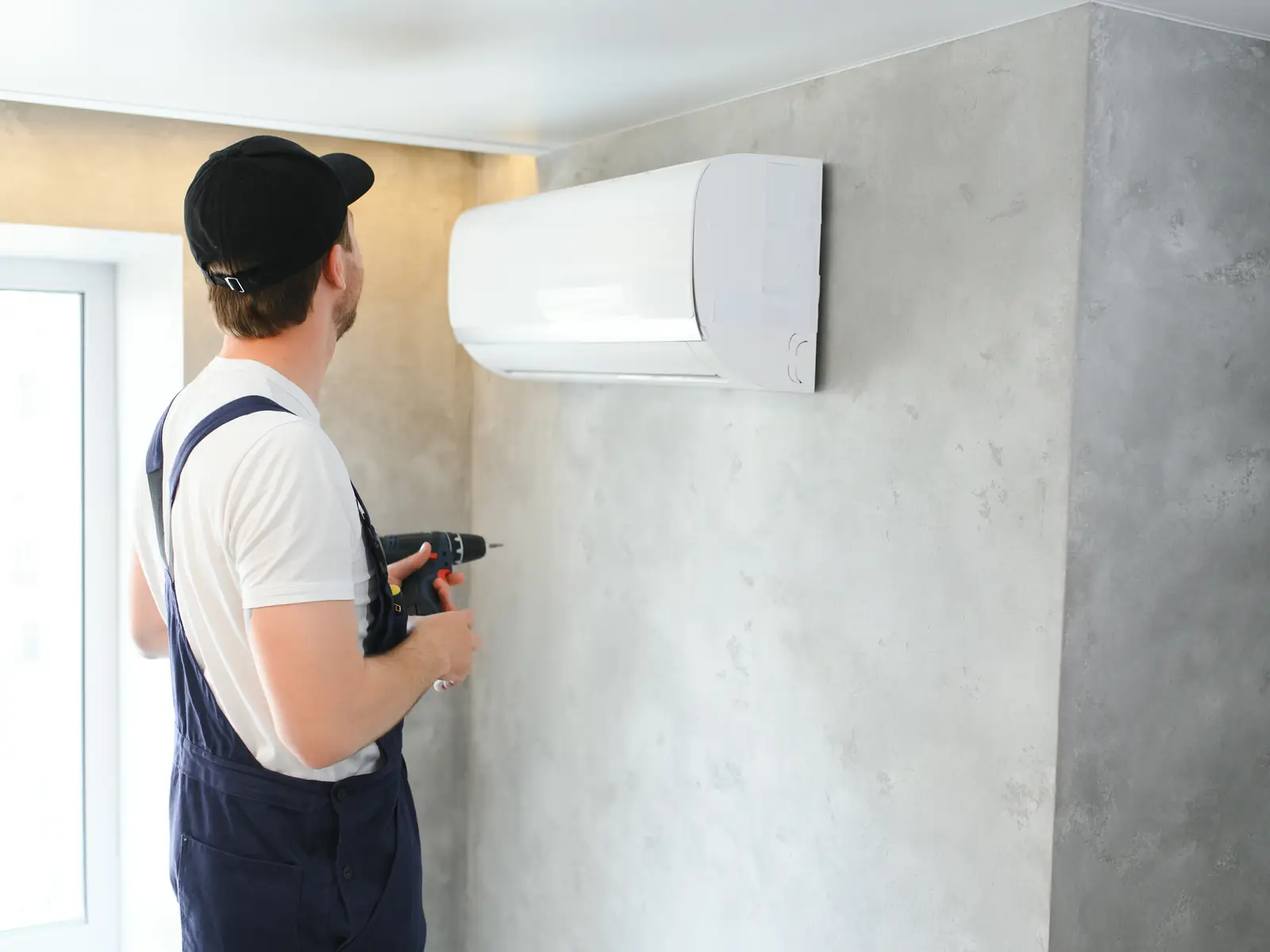 Technicien posant une unité murale de climatisation dans une maison